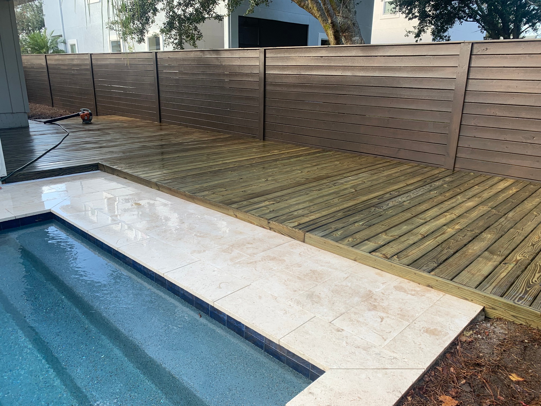 Modern composite and wood pool deck installation with wooden fencing.