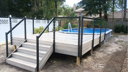 A composite pool deck with a railing and stairs, built around a blue above-ground pool in a backyard.