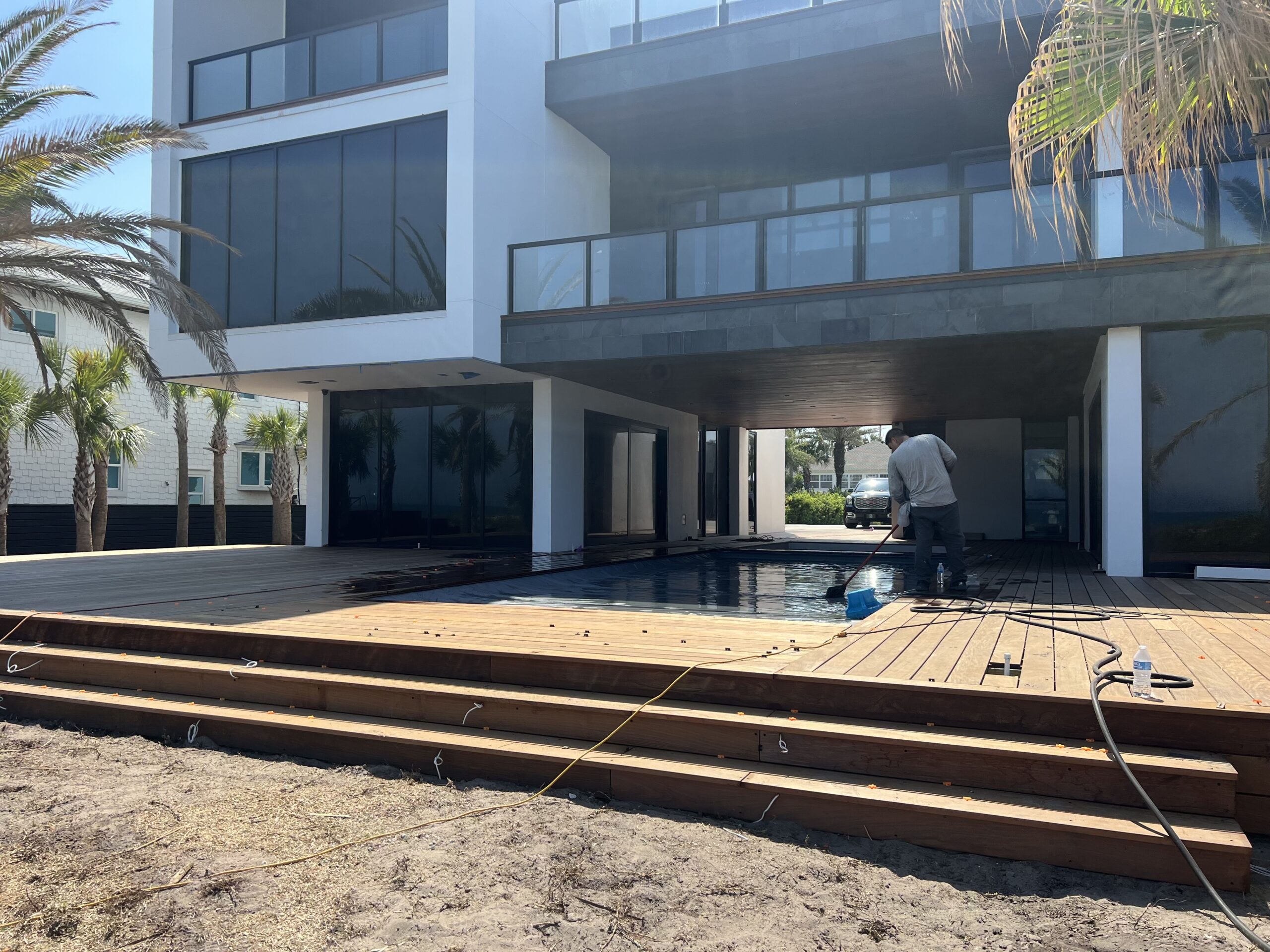 Man cleaning a new wooden pool deck next to a modern home.