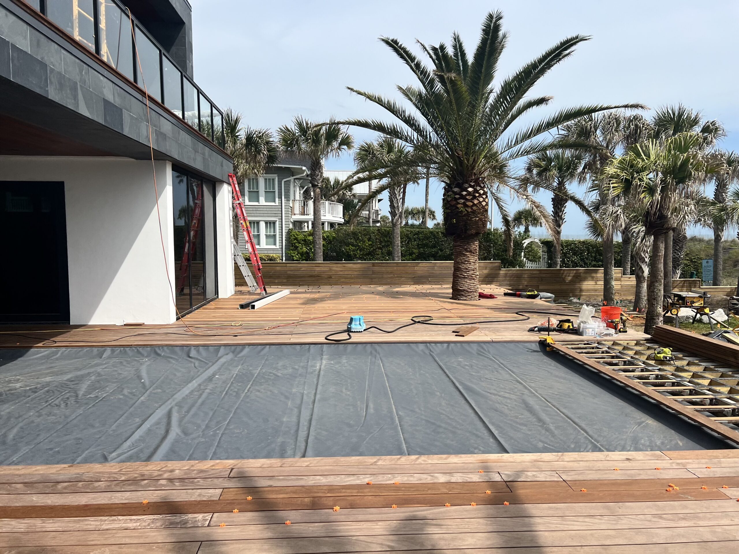 Pool deck under construction, showing composite wood planks, construction tools, and palm trees in Jacksonville, FL.
