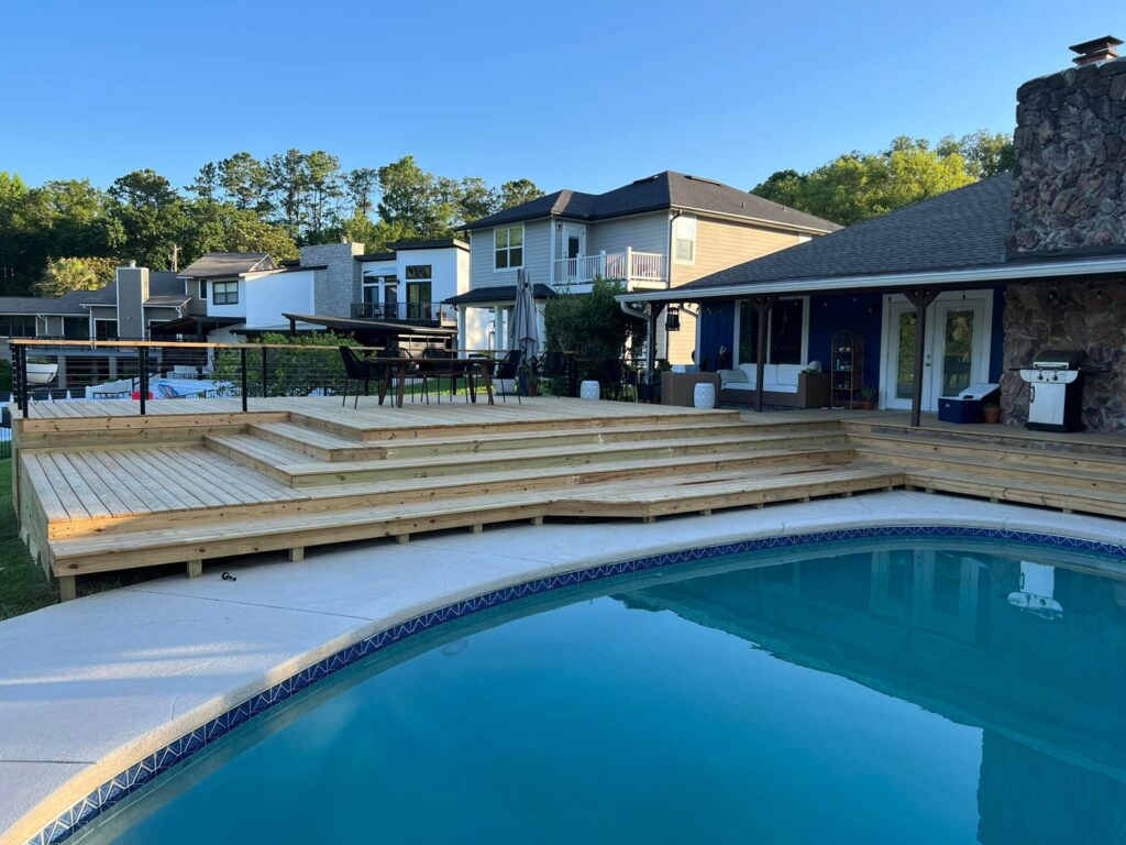 Multi-level wooden pool deck with steps in a backyard, surrounded by houses.