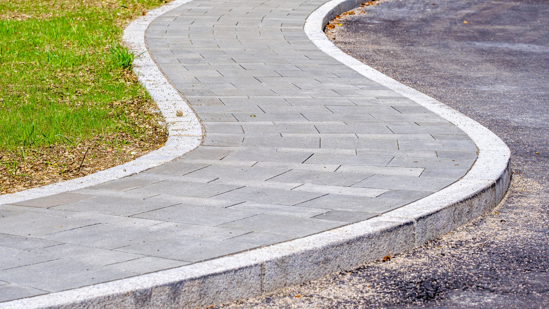 Curved commercial paver walkway beside green landscaping area.