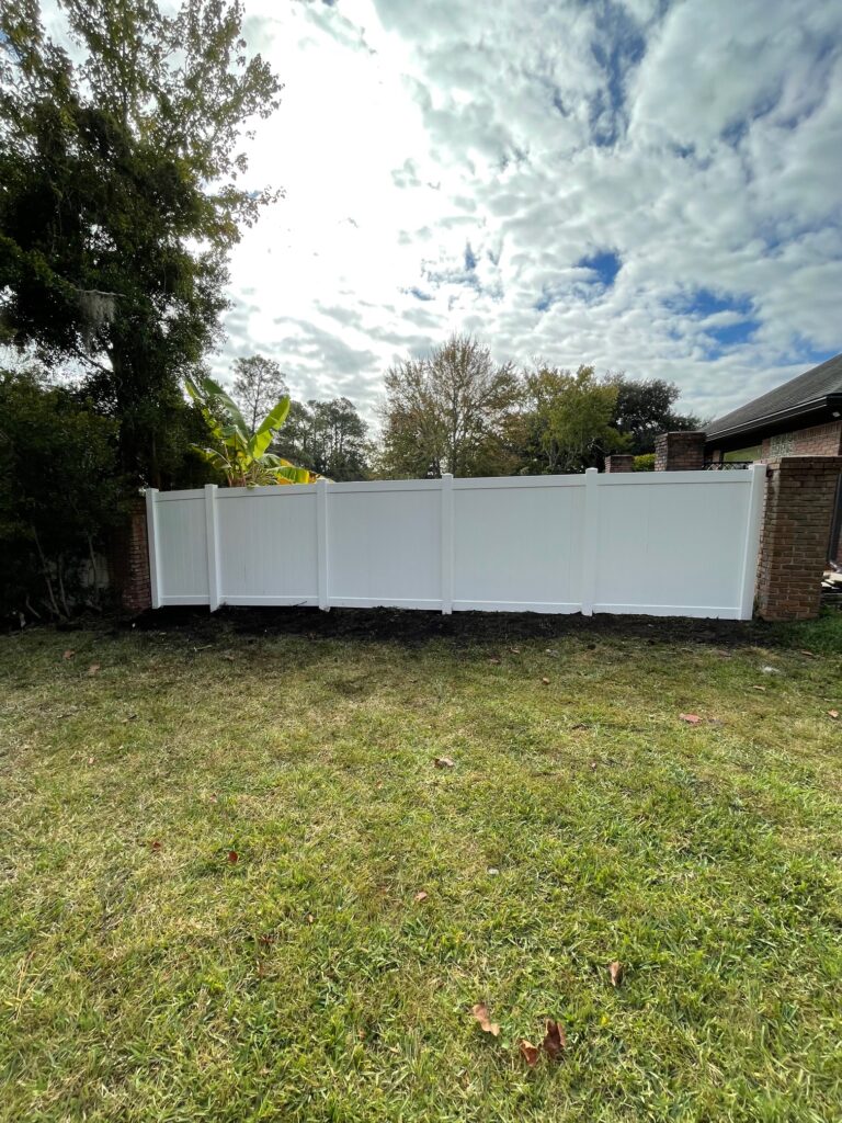 White vinyl fence in backyard with green grass and trees.