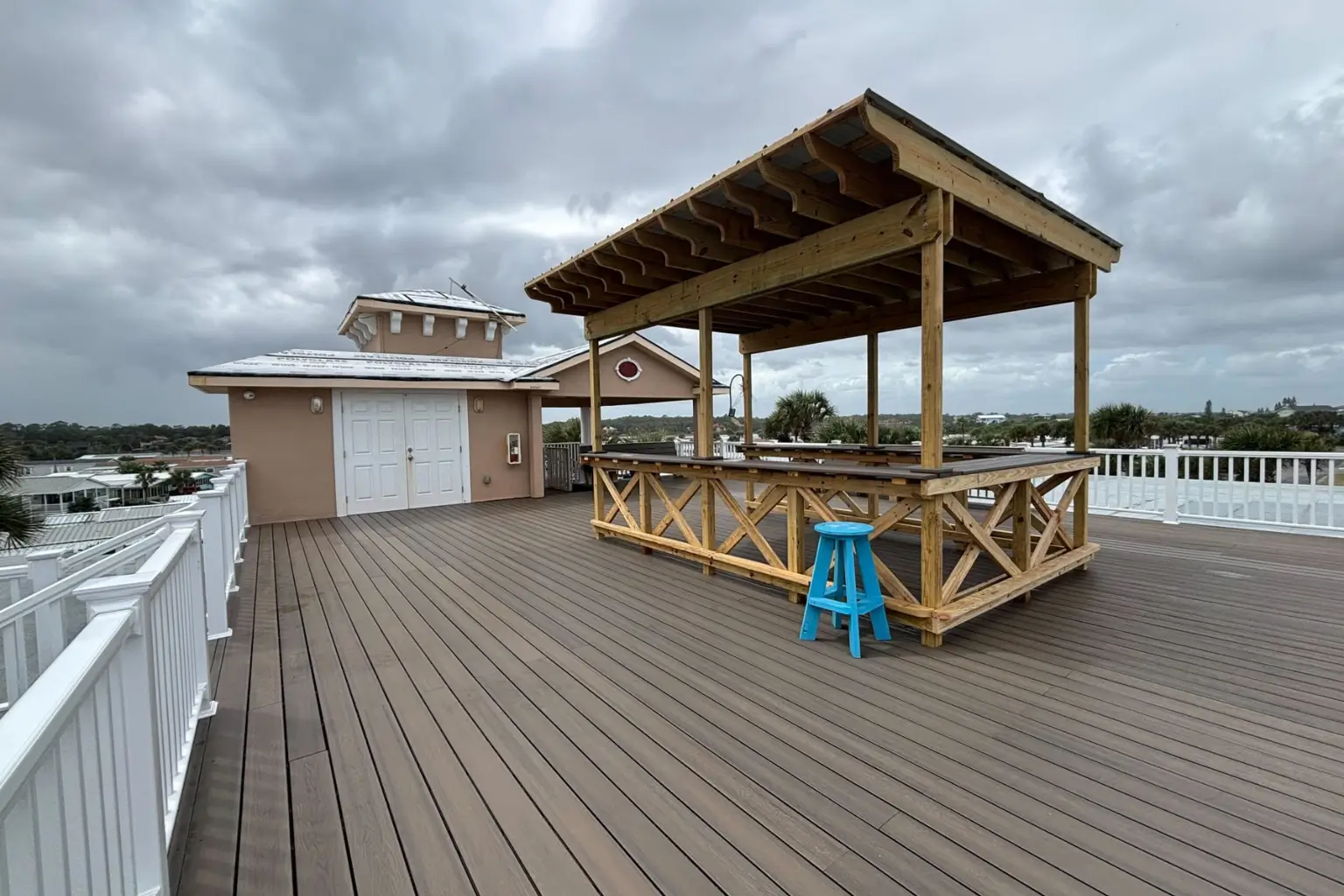 Rooftop deck with wooden bar and blue stool under clouds.