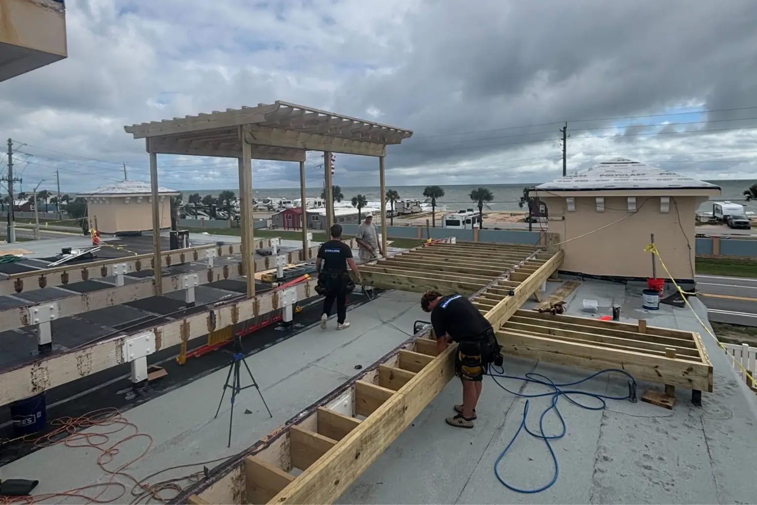 Rooftop deck construction with workers and ocean view.