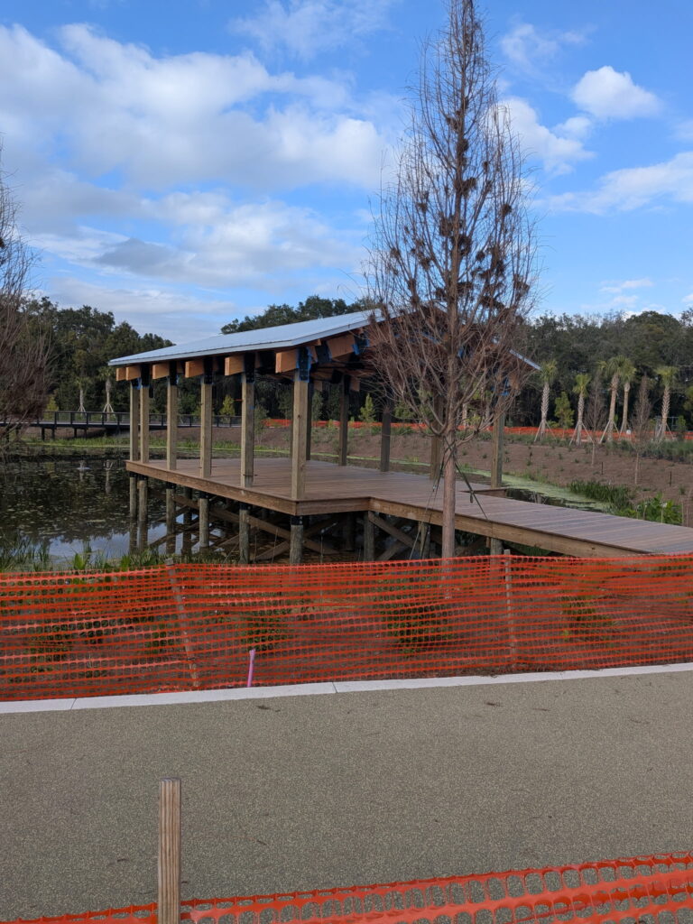 Wooden pavilion over water surrounded by landscaping.